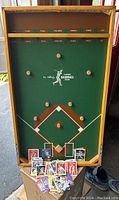 Full view of vertical baseball game board with pegs and labeled outcome slots, several baseball cards spread at base of board