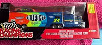 Full boxed set of the Racing Champions 1996 Jeff Gordon transporter truck with attached trailer featuring DuPont and Coca-Cola branding and race car inside, unopened and in original packaging.