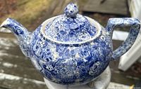 Photo of blue floral chintz ware teapot on outdoor surface, showing lid and spout