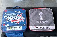 Blue Super Bowl XXXVI cushion with stars and E*TRADE FINANCIAL branding next to black and grey Super Bowl XLVI cushion with Bridgestone branding