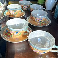 Six handpainted tea cups with floral designs and three matching saucers displayed on a dark wood surface