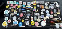 Photo showing a wide assortment of items spread on a table including pins, keychains, mini screwdrivers and bottle openers.