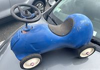 Side view of blue vintage Radio Flyer ride on toy car showing wear and paint loss, black seat and steering wheel.