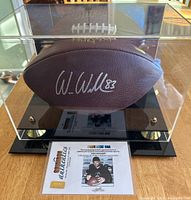 Front view of Wilson NFL football signed by Wes Welker inside acrylic display case with mirrored back and black base with gold accents. Football shows 'W. Welker 83' signature clearly.