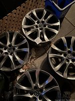 Four metal alloy rims, three Mazda and one Toyota, all approximately size 14, shown with some minor usage marks and dirt