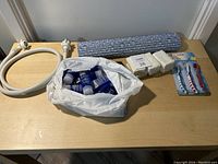 Photo showing all lot items including shower hose, blue hair gel containers in bag, white soap bars, three toothbrushes, and blue bath scrubber.