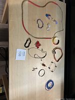 Various jewelry items displayed on a wooden surface including necklace, bracelets, earrings, a pendant, and a watch.
