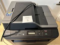 Close-up top view of Brother DCP-L2540DW laser printer showing control panel with LCD and buttons, and part of power cord.