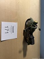 Photo of green motorcycle collectible figurine lying on wooden surface, showing side view with detailed engine and wheels