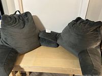 Two gray couch sit-up backrest cushions with arms placed side by side on a wood table, showing overall shape and features.