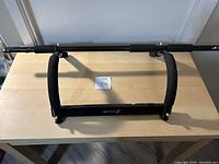 Top-down view of black door frame pull up bar with foam grips, laid flat on wood table.