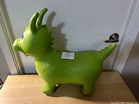 Side view of the green dinosaur/dragon inflatable hopper toy standing on a wooden surface showing shape and horns