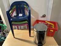 Photo showing three stacked plastic kids chairs in blue, green, and red, a red plastic basket, and a stainless steel pedal trash can.