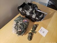 Plastic camouflage tank, bagged green mini soldier toys, and two plastic grenade toys on a cardboard box.