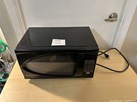 Sharp Carousel microwave oven in black, viewed from the front angle with visible door, control panel, and power cord.