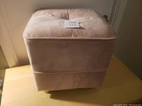 Front-side view of the pink foot stool showing its square shape and soft fabric.