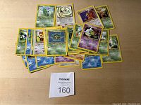 Photo showing an assortment of 28 Pokemon cards laid out on a wooden surface. Cards feature various Pokemon characters from different types including water, grass, psychic etc. All cards appear to be in excellent condition with clear artwork and minimal edge wear.