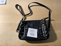 Front view of the black leather purse with metal studs and shoulder strap on a flat surface, showing zipper closure and stud details.