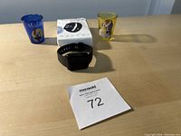Lot overview showing two shot glasses, boxed black smart watch, and charger cable