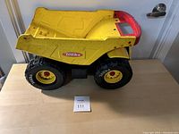 Side and top views of the yellow metal Tonka dump truck showing the large black Tonka-branded wheels and red rear edge of the dump bed.