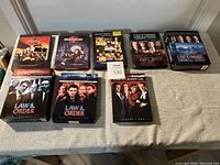Photo of nine DVD box sets of various TV series including multiple Law & Order series and Third Watch seasons.