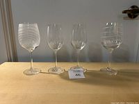 Photo of four wine glasses arranged in a row on a flat surface, showing two glasses with white swirl patterns and two plain glasses.