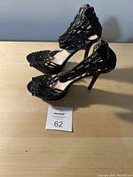 Side view of a pair of women's black high-heeled dress shoes with beaded decoration and strappy design on heel area.