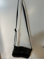 Black small crossbody purse with adjustable strap hanging on wall showcasing front with zipper pocket