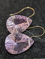 Close-up photo of one earring showing teardrop-shaped faceted amethyst stone with a gold hook