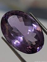 Close-up photo of the oval faceted amethyst held by tweezers, showing its purple color and clarity.