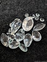 Clear to light blue aquamarine gemstones of various faceted shapes including pear, oval, round and marquise cuts on a dark background.