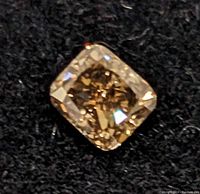 Close-up of the natural champagne color diamond showing faceted cushion cut shape and internal inclusions on a black fabric background.