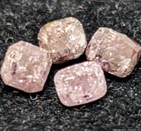 Close-up photo of four rough-cut deep pink diamonds on black fabric.