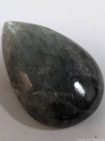 Polished pear-shaped labradorite gemstone showing dark gray color and iridescent sheen