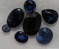 Close-up of seven sapphire gemstones on white background showing variety of cuts and sizes.