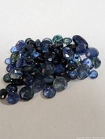 Pile of loose genuine blue sapphire gemstones on white surface, showing various sizes and cuts.
