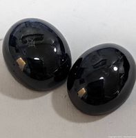 Two oval-shaped polished star sapphire gemstones viewed from an angle, showing deep dark blue to black coloring and reflective surfaces.