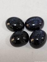 Four oval cabochon cut dark star sapphire stones, polished with visible star-shaped asterism effect.