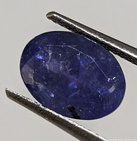 Close-up of oval cut tanzanite gemstone held by tweezers showing color and internal characteristics.