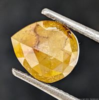 Close-up frontal view of pear-shaped yellow diamond held by tweezers