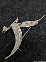 Silver brooch shown on a black background, viewed from front with visible mixed textured and smooth finishes.