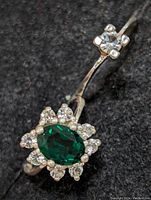 Close-up front view of the ring featuring an oval green stone surrounded by clear stones on a silver band