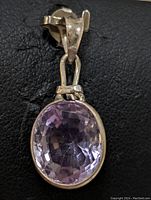 Front view of sterling silver pendant with oval amethyst, showing faceted surface and bail.