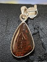 Close-up front image of triangular ammolite pendant with silver setting showing the gemstone's red and orange iridescent colors.