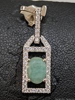 Front view of the sterling silver pendant featuring an oval green emerald gemstone and a rectangular clear stone frame.