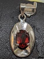 Close-up front view of oval sterling silver pendant with faceted garnet stone in center.