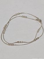 Sterling silver necklace with small silver bead accents distributed along a thin chain, displayed laid out flat.