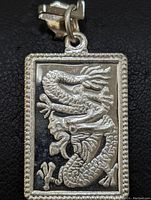 Close-up front view of rectangular sterling silver pendant with detailed dragon design and beaded border.