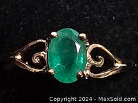 Close-up of ring showing front view of oval emerald and gold swirl details on split shank.