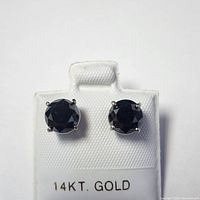 Front view of two round black diamond studs on white display card marked ‘14KT. GOLD’